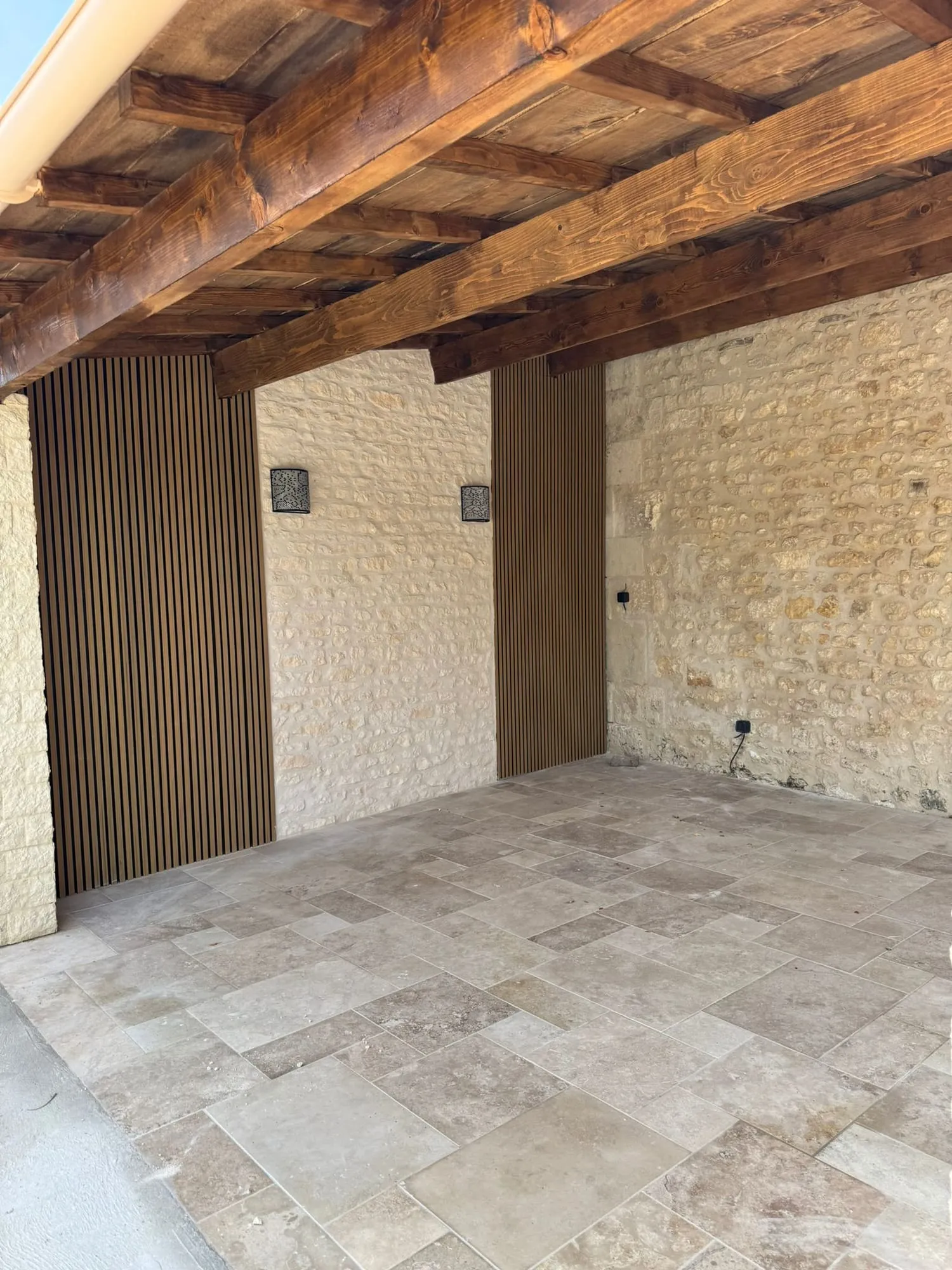 Préau à charpente bois vernie, mur en pierre calcaire rejointoyé et sol en travertin.