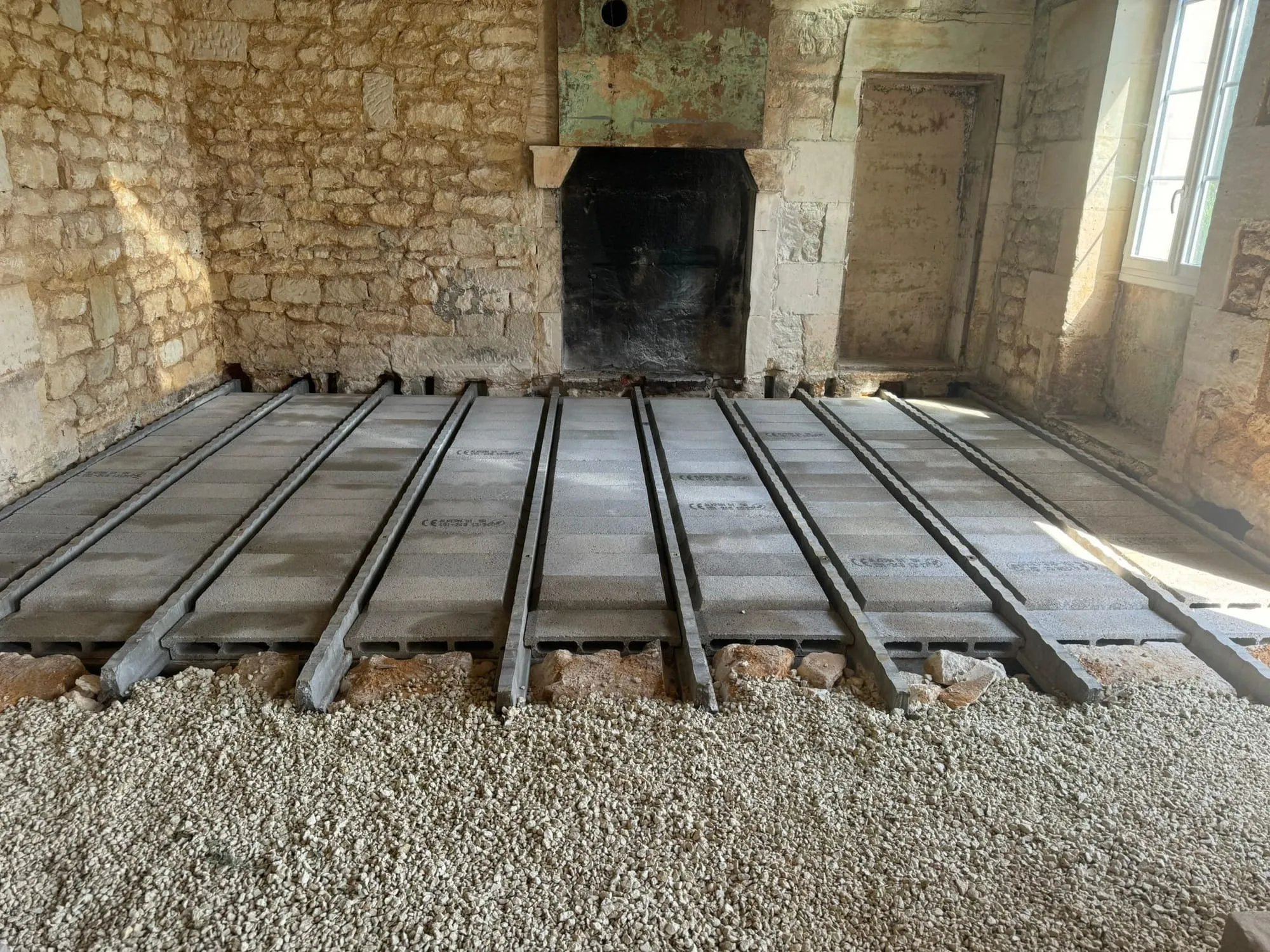 Poutrelles et hourdis béton posés sur des plots de pierre, dans une pièce ancienne avec cheminée.