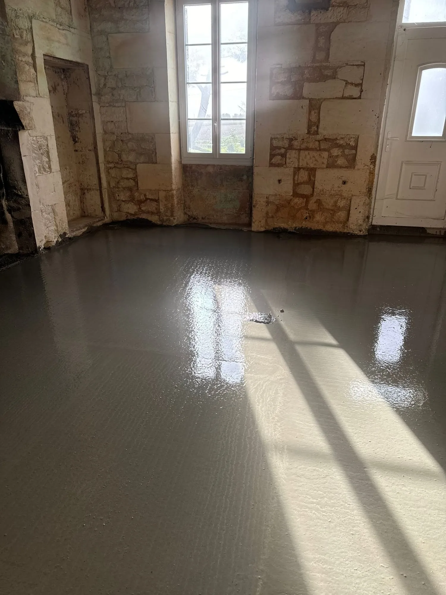 Dalle béton fraîchement coulée et lissée, réfléchissant la lumière d'une fenêtre, entre des murs en pierre de taille.